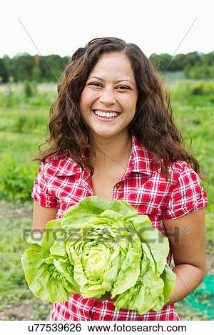 Stock Photograph - Portrait of young woman holding cabbage in allotment. Fotosearch