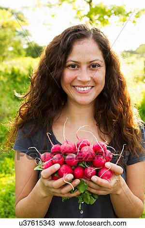 Stock Image - Portrait of young woman holding crop of radishes in allotment. Fotosearch