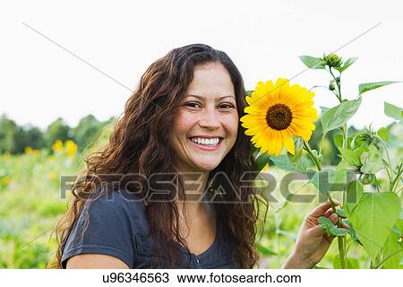 Stock Image - Portrait of young woman with yellow sunflowers in allotment. Fotosearch