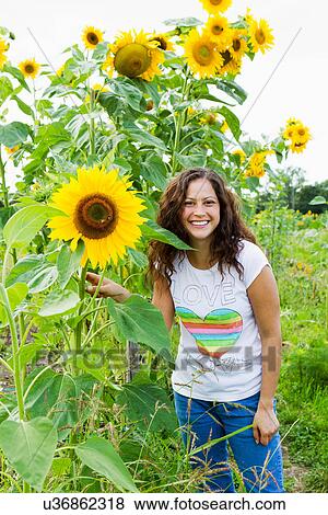 Stock Photo - Portrait of young woman with yellow sunflowers in allotment. Fotosearch