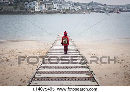 Stock Photography - Rear view of boy standing on pier overlooking sea. Fotosearch
