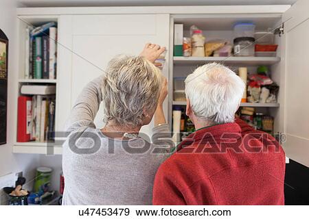 Stock Photo - Senior couple checking kitchen cupboards. Fotosearch
