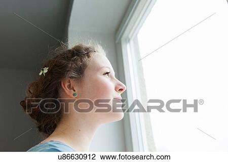 Stock Image - Teenage girl looking out of window, close up. Fotosearch