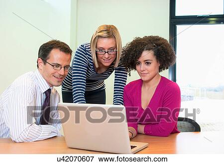Stock Photo - Three colleagues working on laptop in office. Fotosearch