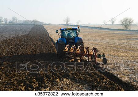 Stock Image - Tractor ploughing the ground of field. Fotosearch