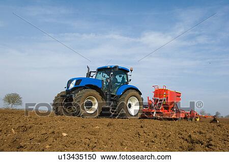 Stock Image - Tractor pulling equipment to plant seeds in field. Fotosearch