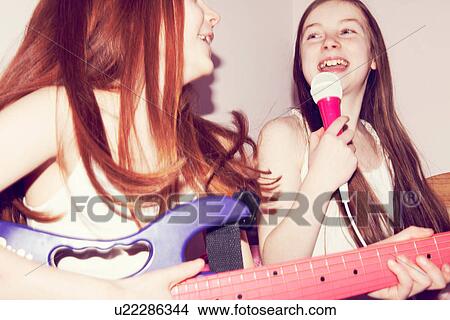 Picture - Two girls playing guitar and singing into microphone in bedroom. Fotosearch