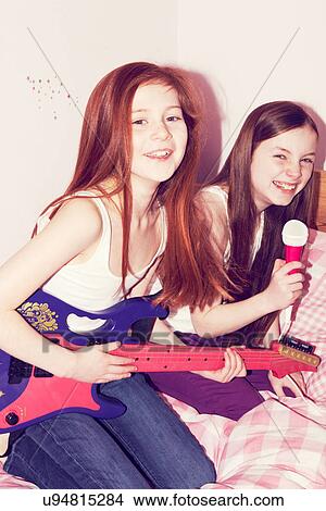 Picture - Two girls playing guitar and singing into microphone in bedroom. Fotosearch
