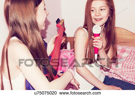 Two girls playing guitar and singing into microphone in bedroom View Large Photo Image Stock Image - Two girls playing guitar and singing into microphone in bedroom. Fotosearch