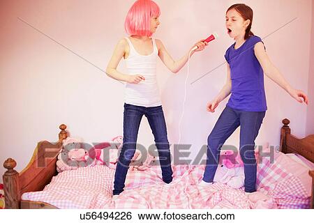 Two girls standing on bed singing into microphone View Large Photo Image Stock Photograph - Two girls standing on bed singing into microphone. Fotosearch