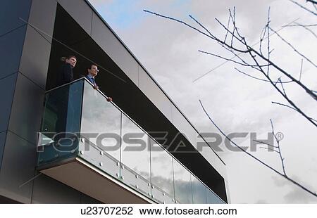 Stock Image - Two office colleagues on balcony, low angle. Fotosearch