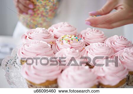 Stock Image - Woman decorating cupcakes with sugar sprinkles. Fotosearch