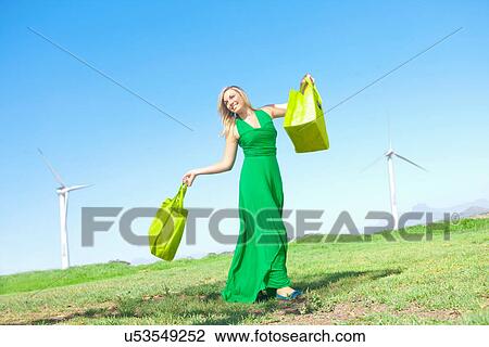 Stock Image - Woman in field with green shopping bags. Fotosearch