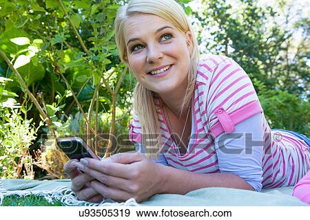 Woman lying on blanket in garden using cell phone View Large Photo Image Stock Photo - Woman lying on blanket in garden using cell phone. Fotosearch