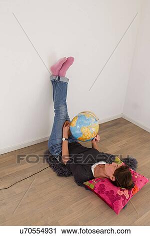 Stock Image - Woman lying on floor of empty room holding globe. Fotosearch