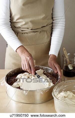 Stock Image - Woman making chocolate cake, spreading cream. Fotosearch