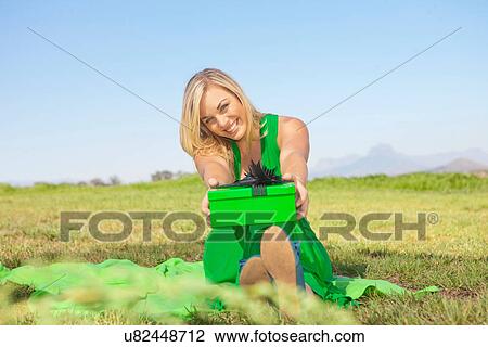 Woman sitting in field offering green gift View Large Photo Image Stock Image - Woman sitting in field offering green gift. Fotosearch