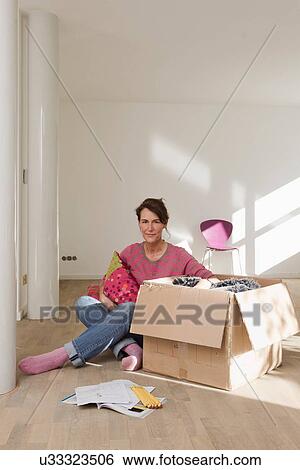 Stock Photograph - Woman sitting on wooden floor unpacking cardboard box. Fotosearch