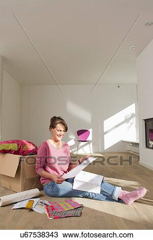 Stock Image - Woman sitting on wooden floor with box reading document. Fotosearch