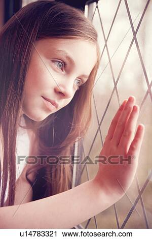Stock Image - Young girl looking though window. Fotosearch