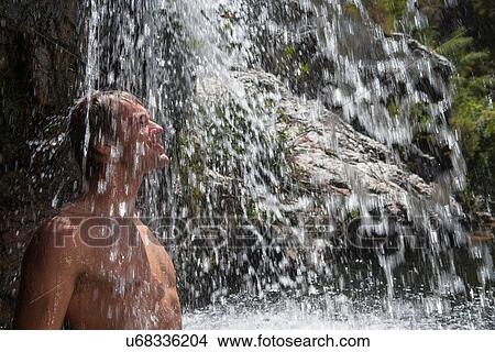Young man standing under waterfall View Large Photo Image Picture - Young man standing under waterfall. Fotosearch