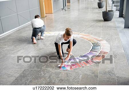 Stock Image - Young woman and mid adult man arranging swatches on lobby floor. Fotosearch