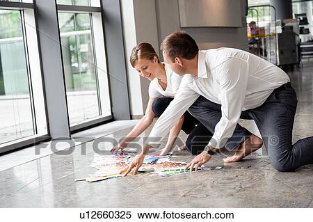Stock Photography - Young woman and mid adult man arranging swatches on lobby floor. Fotosearch