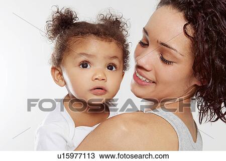 Stock Image - Young woman holding baby daughter in studio. Fotosearch