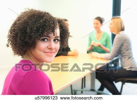 Stock Image - Young woman in office with colleagues in background. Fotosearch