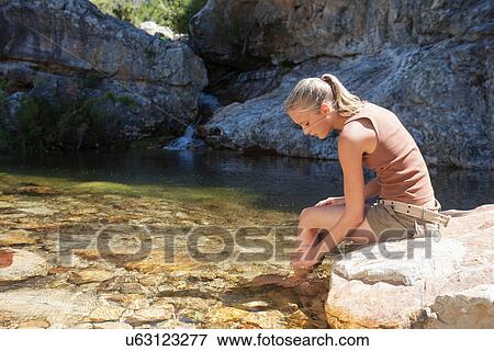 Stock Photo - Young woman sitting on rock and bathing in stream. Fotosearch