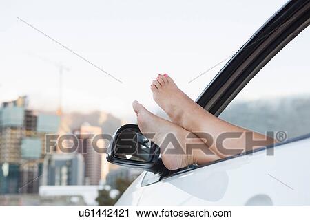 Stock Image - Young woman with feet up through car window. Fotosearch