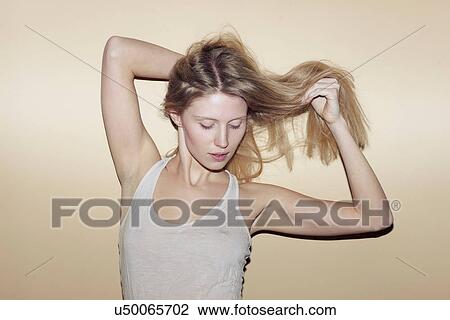 Stock Image - Young woman with hands in long blonde hair. Fotosearch