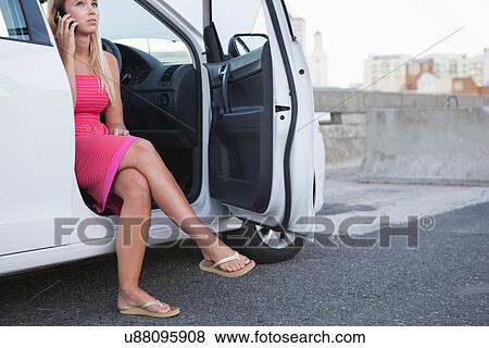 Stock Photo - Young women sitting in car with door open on cell phone. Fotosearch