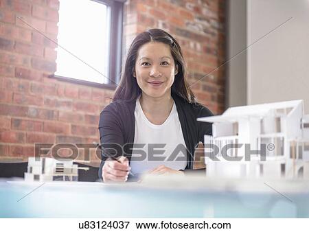 Stock Photo - Architect working at desk in office with model of buildings. Fotosearch