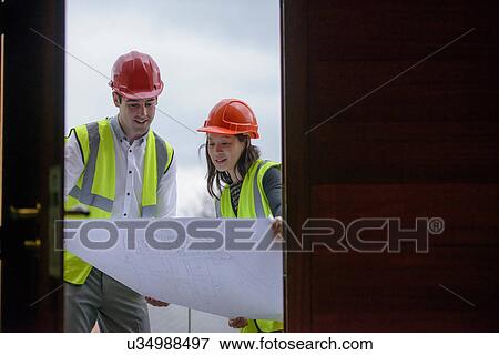 Stock Photo - Architects in hard hats and reflective workwear inspecting plans. Fotosearch