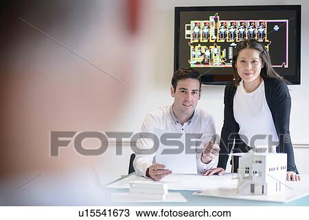 Stock Image - Architects making presentation in boardroom with model building. Fotosearch