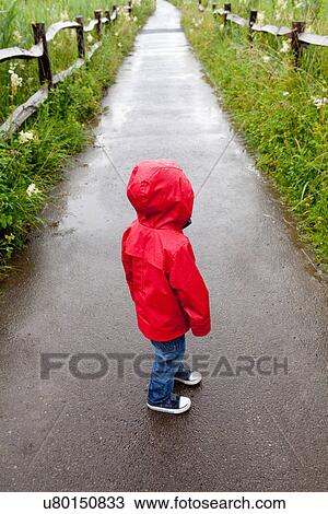 Stock Image - Back view of toddler standing on pathway in red raincoat. Fotosearch