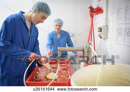 Picture - Baker guiding trainee in adding cream to cakes covered with jam. Fotosearch