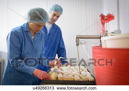Stock Image - Baker guiding trainee in adding cream to freshly baked cakes. Fotosearch