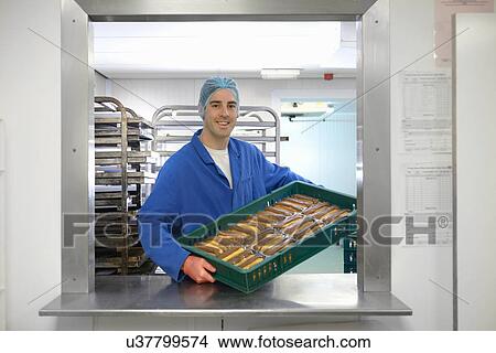 Baker holding tray of freshly baked chocolate eclairs in small bakery View Large Photo Image Picture - Baker holding tray of freshly baked chocolate eclairs in small bakery. Fotosearch