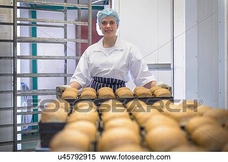 Stock Photography - Baker holding tray of freshly baked bread, portrait. Fotosearch