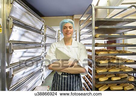 Picture - Baker standing by racks of baked pastries, portrait. Fotosearch