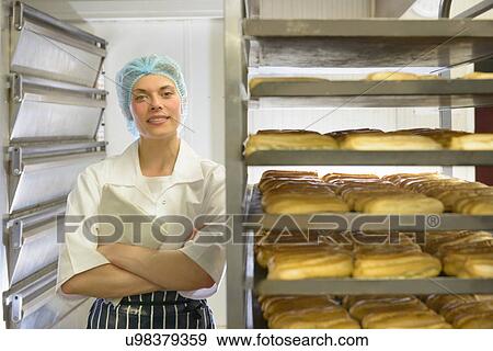 Stock Photo - Baker standing by racks of baked pastries, portrait. Fotosearch