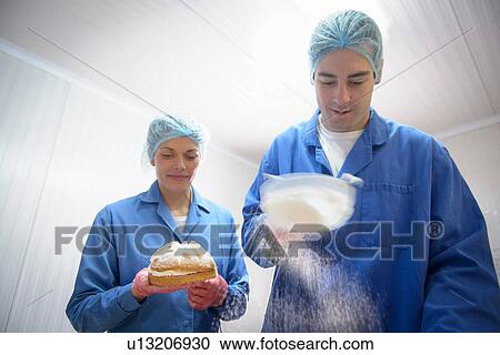 Stock Image - Bakers dusting sugar onto baked cakes. Fotosearch