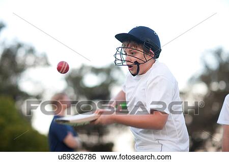 Stock Photograph - Boy practising hitting cricket ball with bat. Fotosearch