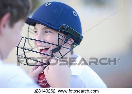 Stock Image - Boy putting cricket helmet on another boy. Fotosearch