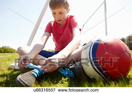 Stock Photo - Boy sitting on field tying shoe lace. Fotosearch