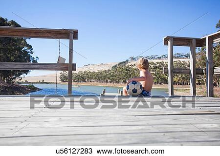 Stock Image - Boy sitting on pier with football. Fotosearch