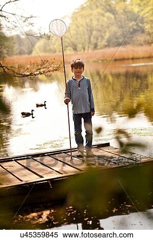 Stock Photography - Boy standing on pier holding fishing nets, portrait. Fotosearch