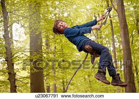 Boy swinging on rope in forest View Large Photo Image Stock Image - Boy swinging on rope in forest. Fotosearch